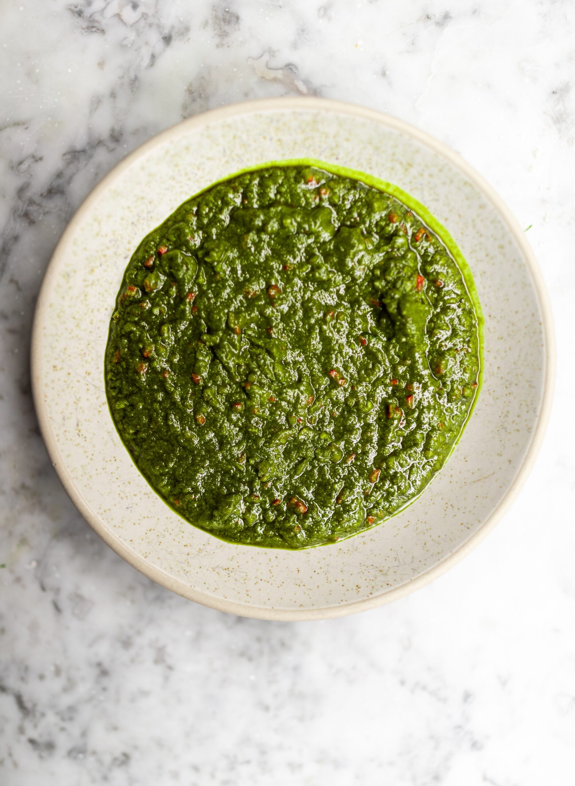 Overhead shot of beef fat chimichurri in a white bowl on a marble countertop