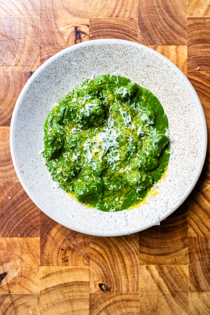 Overhead shot of British pesto sauce and gnocchi in a white bowl on a wooden chopping board