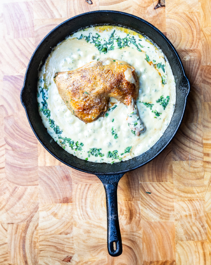 Overhead shot of a mustard velouté with a roasted chicken leg in the middle, all in a cast iron pan on a wooden background