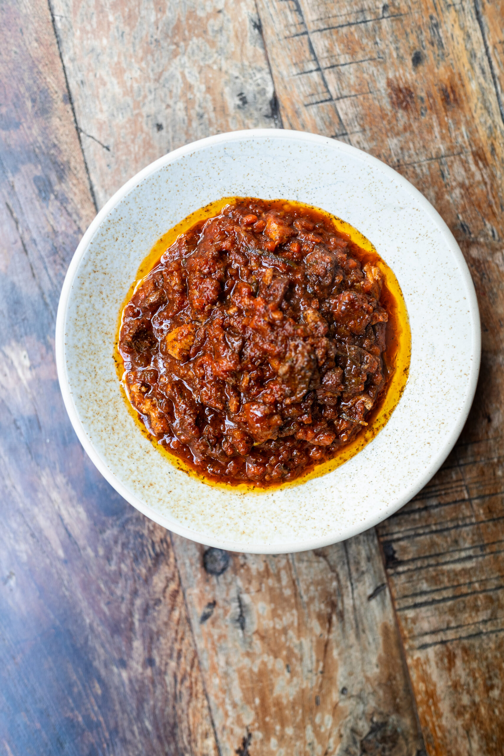 Overhead shot of pork and beef ragu in a white bowl on a wooden table