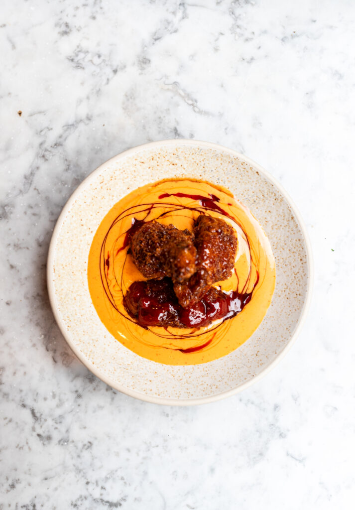 Fallow sriracha butter sauce in a white bowl with chicken wings in the centre.