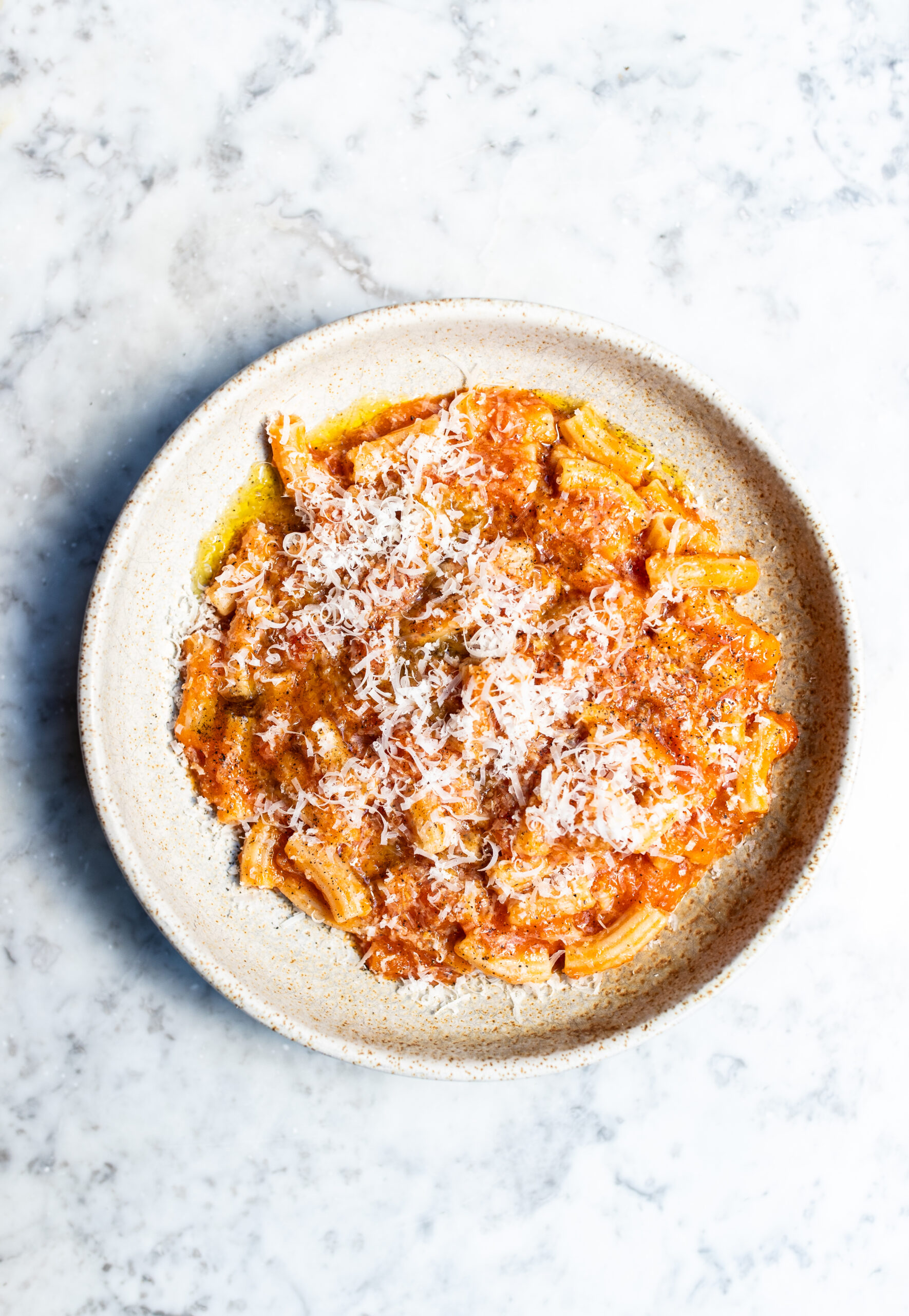 Overhead shot of homemade tomato sauce with pasta in a white bowl on a marble tabletop
