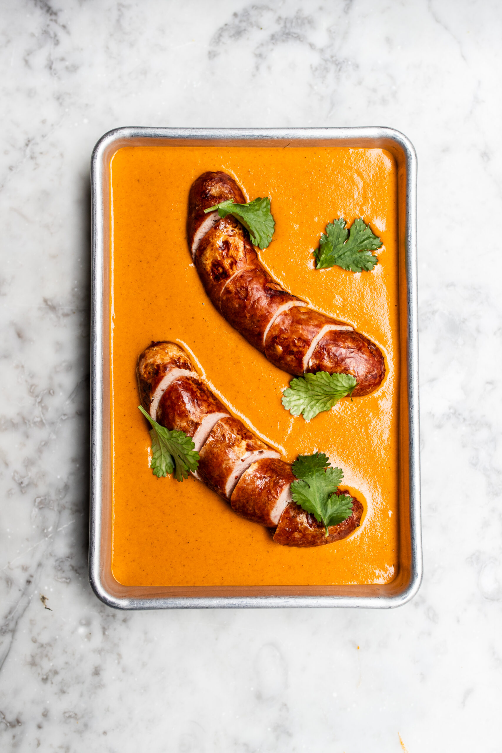 Overhead shot of chip shop curry sauce in a steel flat tray with two sliced sauces sitting the in the middle.