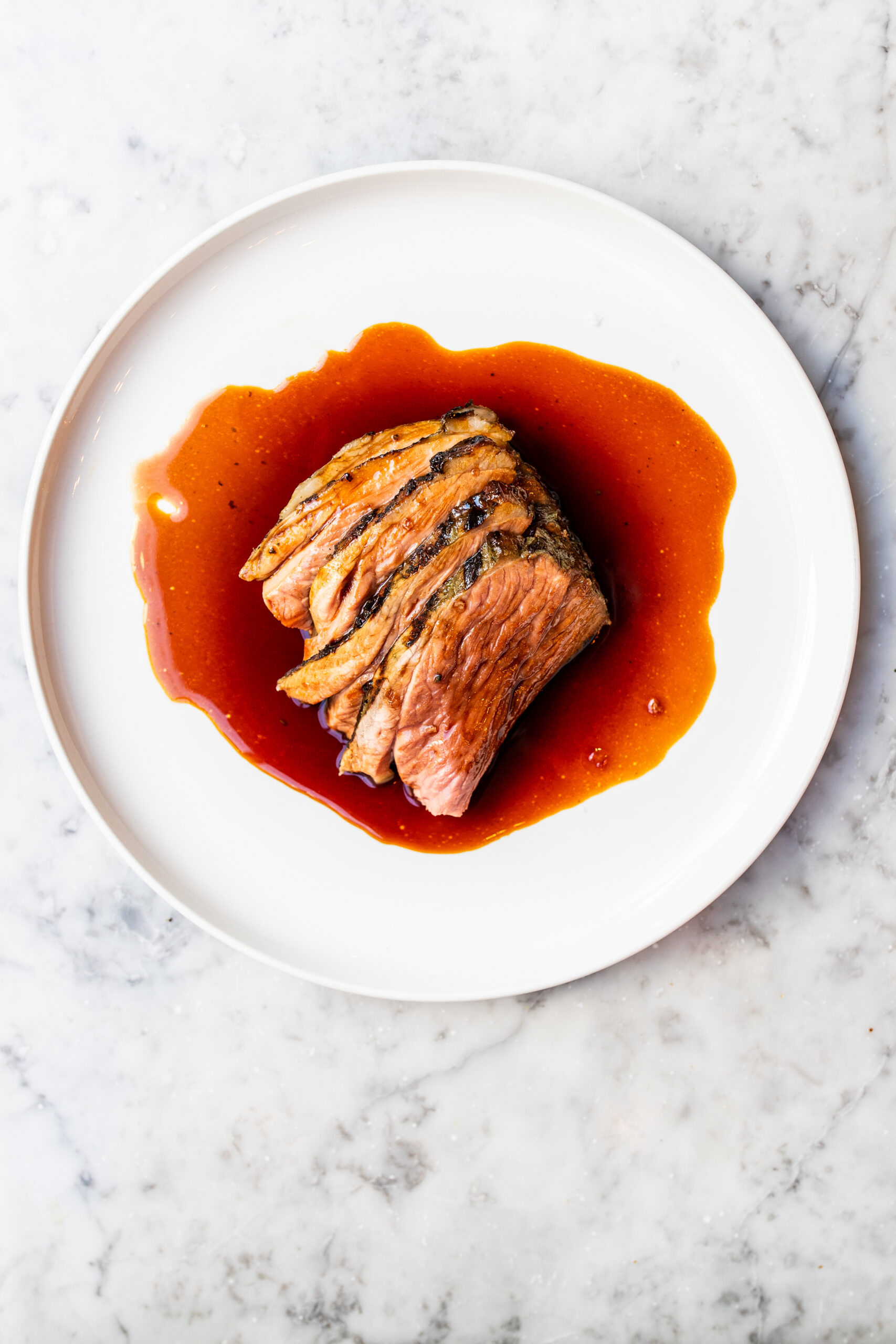 Overhead view of red wine sauce over a steak on a white plate and marble countertop