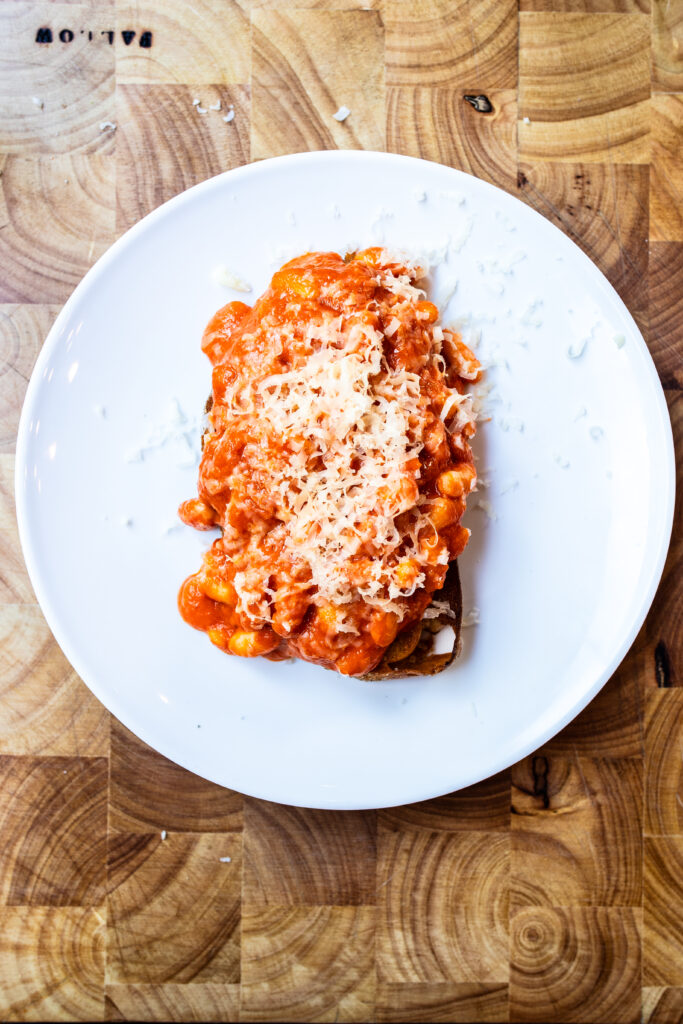 Overhead shot of homemade beans on toast on a white plate and wooden board