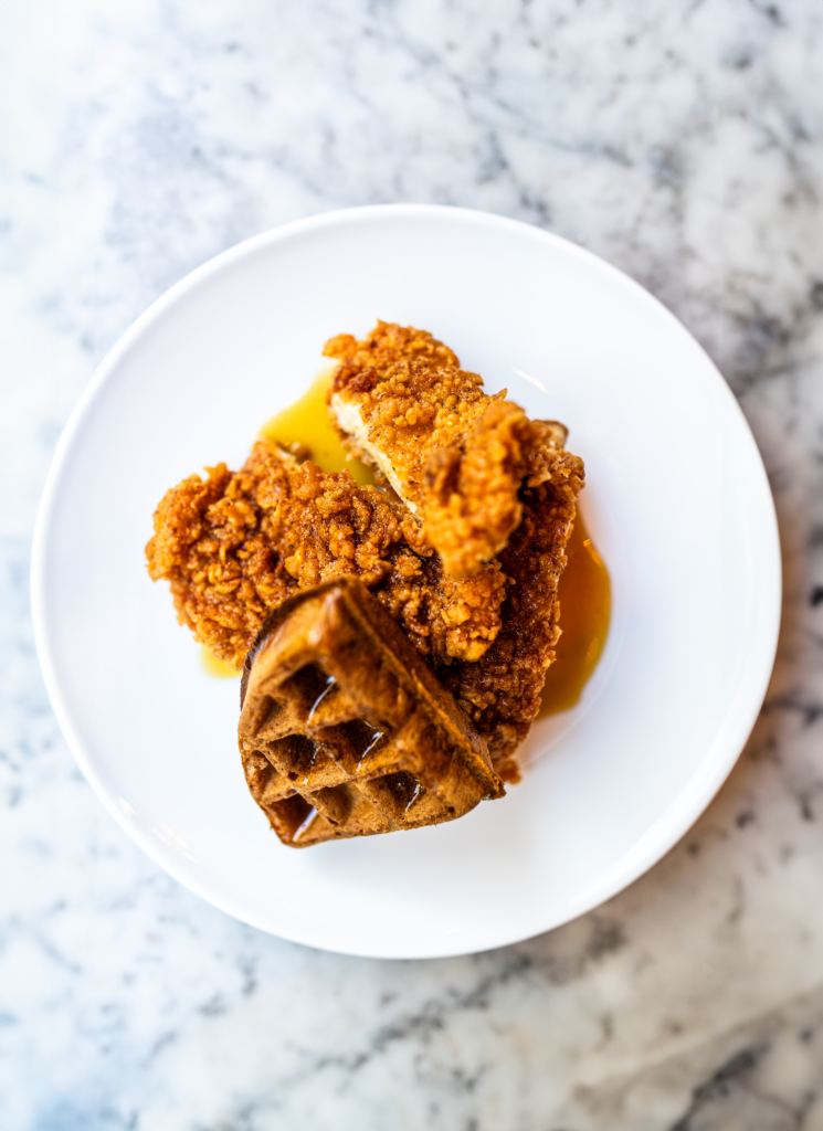 Overhead shot of chicken and waffles with maple syrup on a white plate and marble countertop