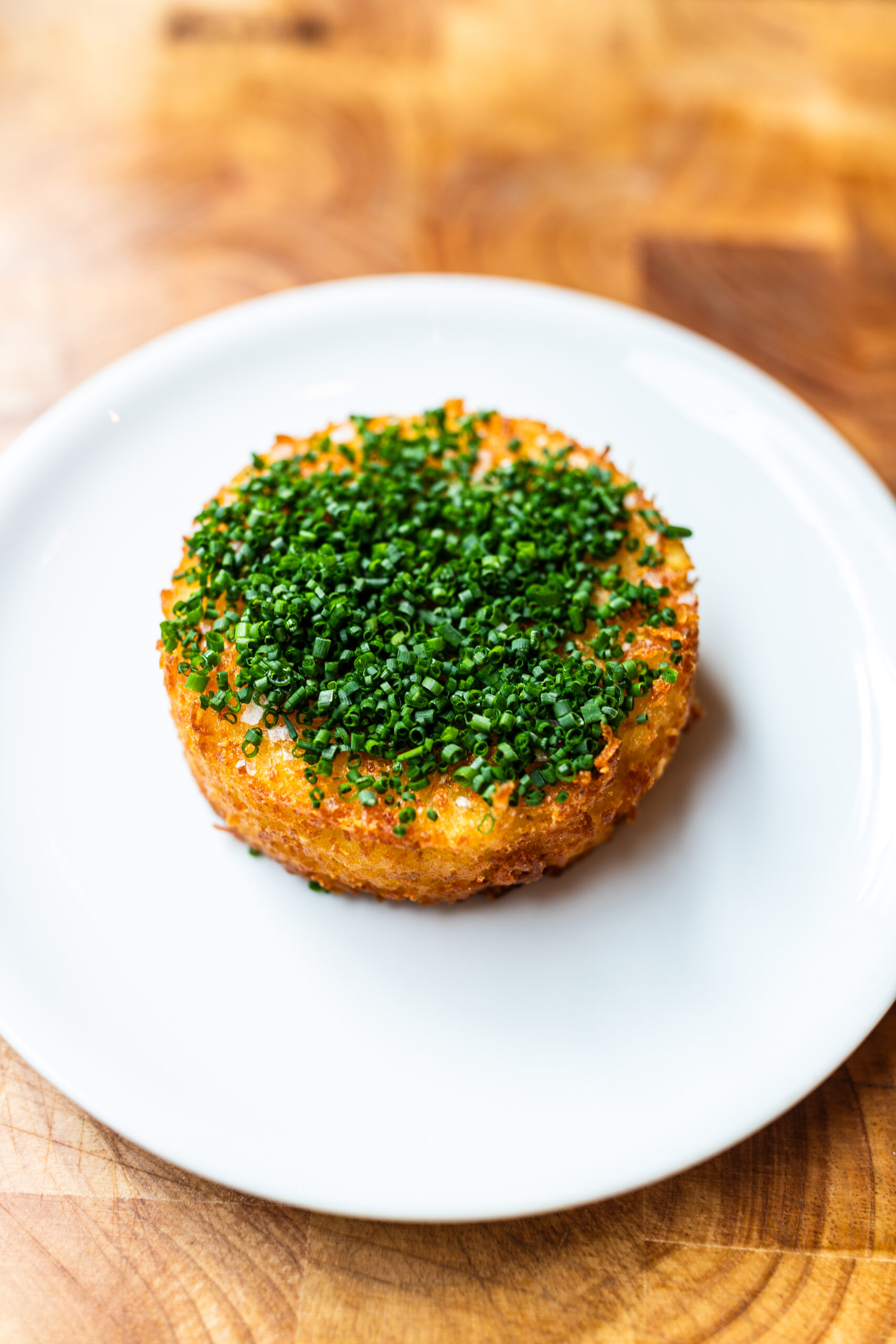 Egg yolk hash brown topped with chopped chives on a white plate and wooden background