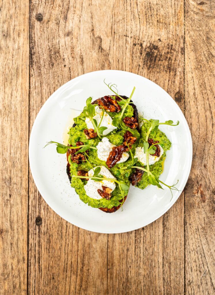 Overhead shot of no avo toast with goats’ curd and topped with caramelised walnuts and pea shoots
