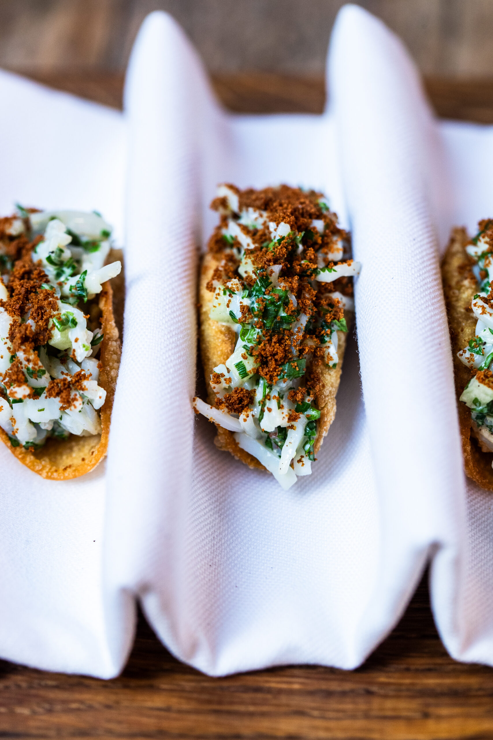 An overhead image of crab tacos on a folded cloth on a wooden chopping board.