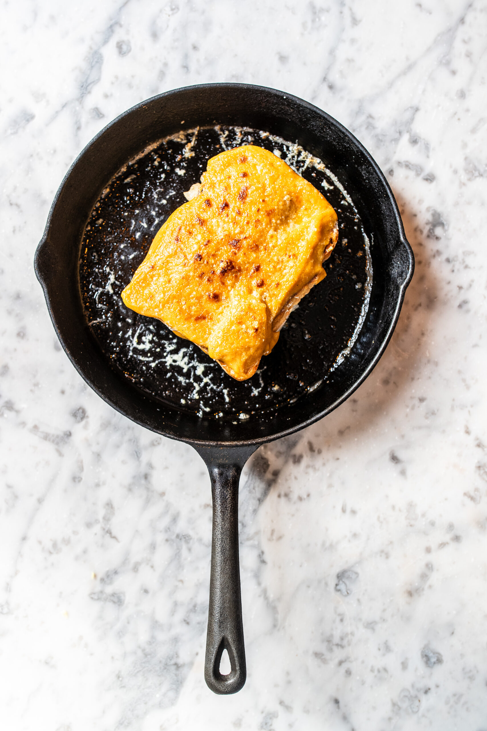 Overhead shot of a croque-monsieur rarebit in a cast iron pan on a marble table