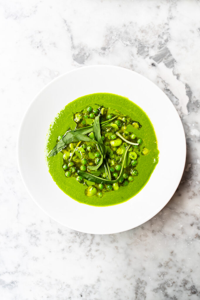An overhead shot of a white bowl of green tomato gazpacho on a white marble table.
