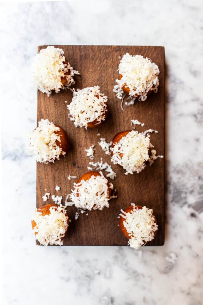 An overhead of mini cheese doughnuts topped with grated cheese on a wooden chopping board on a marble table.