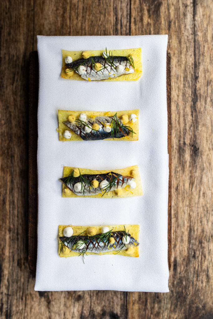 An overhead shot of sardine sashimi on a rectangular white plate on a wooden table.