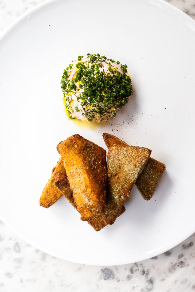 An image of pieces of panisse with a side of taramasalata on a white plate on top of a white marble table
